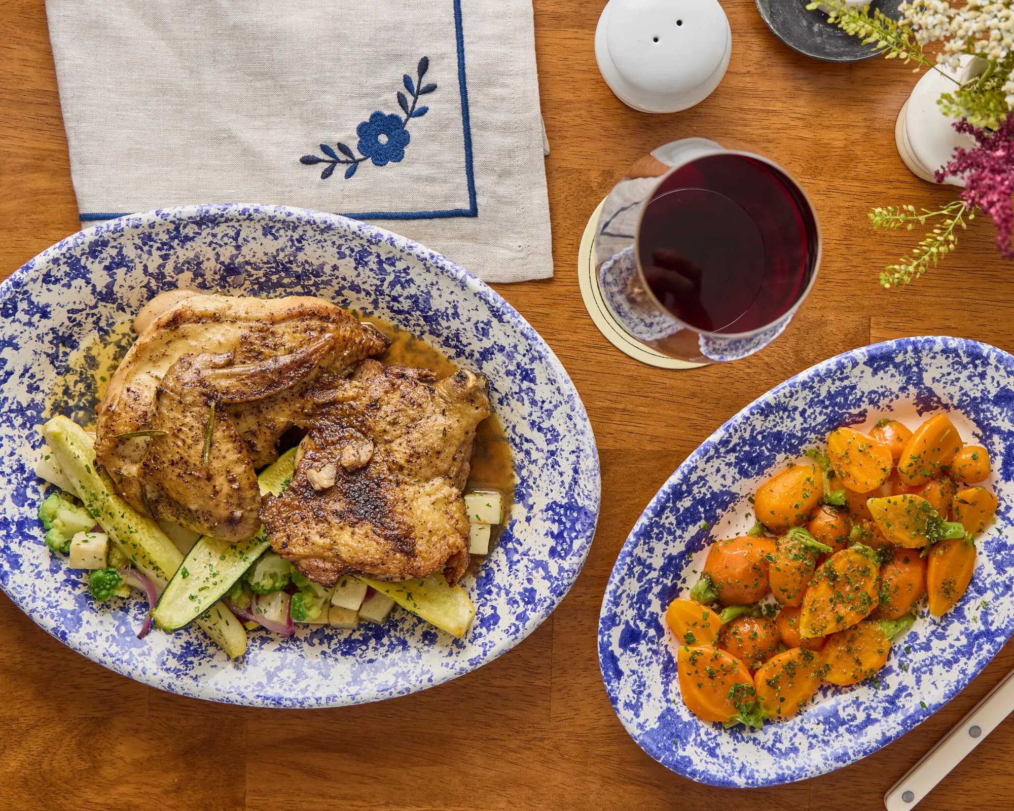 Roast chicken with summer vegetables and a platter of glazed carrots on blue spatterware at The Feathers, with a glass of red wine.